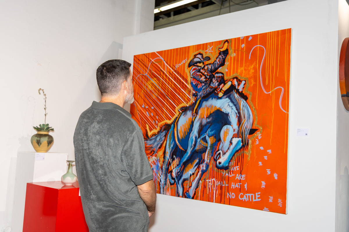 A visitor studies an orange painting of a bucking bronco